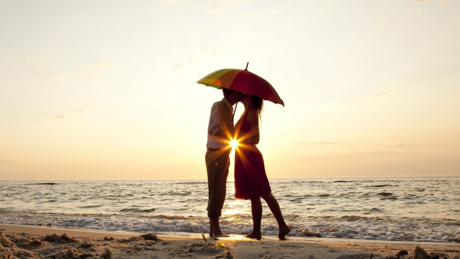 Fondo de pantalla Couple Kissing Under Umbrella At Sunset On Beach 1600x900