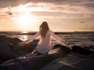 Sfondi Girl Sitting On Stones On Sea Coast 320x240