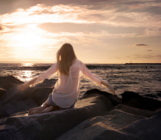 Kostenloses Girl Sitting On Stones On Sea Coast Wallpaper für iPad