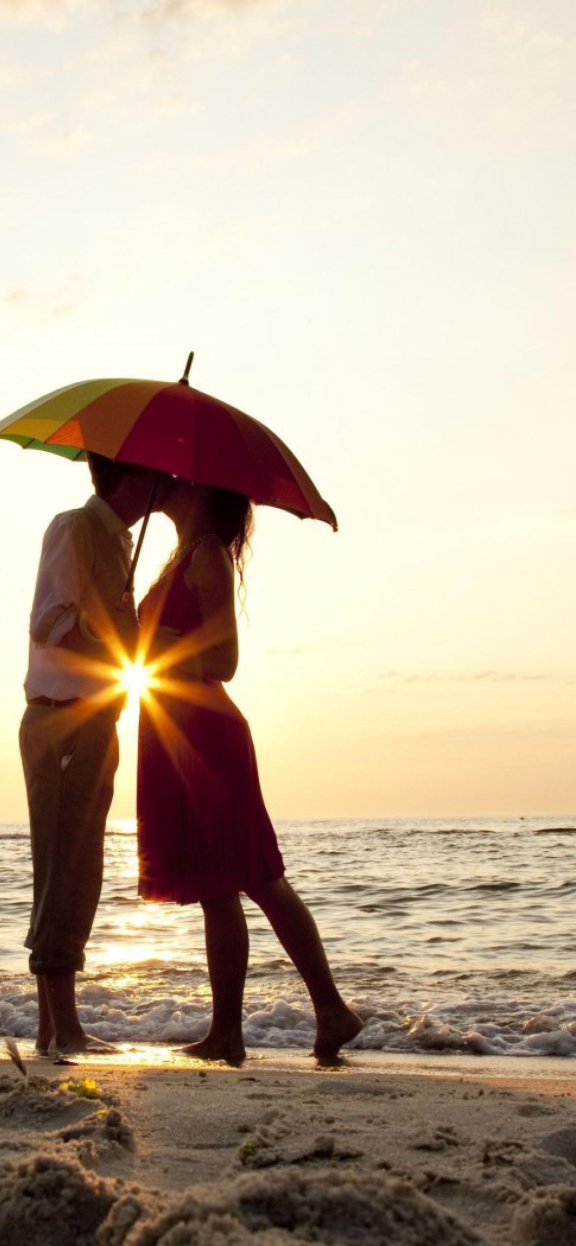 Fondo de pantalla Couple Kissing Under Umbrella At Sunset On Beach 1170x2532