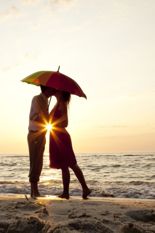 Couple Kissing Under Umbrella At Sunset On Beach wallpaper 320x480