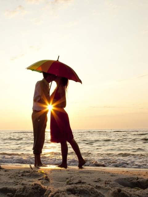 Das Couple Kissing Under Umbrella At Sunset On Beach Wallpaper 480x640