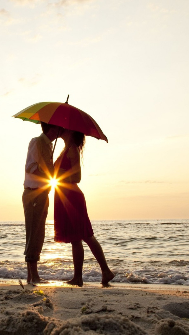 Couple Kissing Under Umbrella At Sunset On Beach wallpaper 640x1136