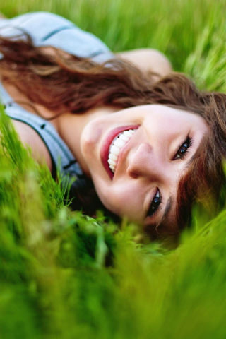 Smiling Girl Lying In Green Grass wallpaper 320x480