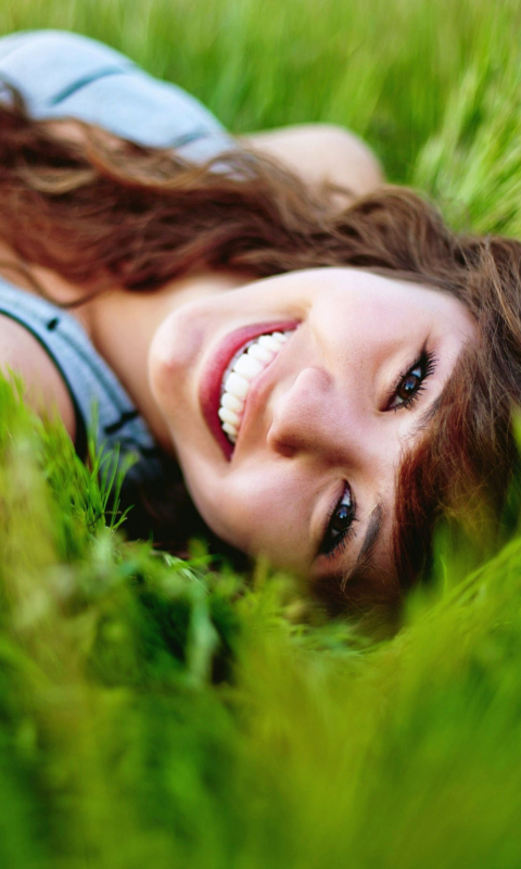 Smiling Girl Lying In Green Grass wallpaper 480x800