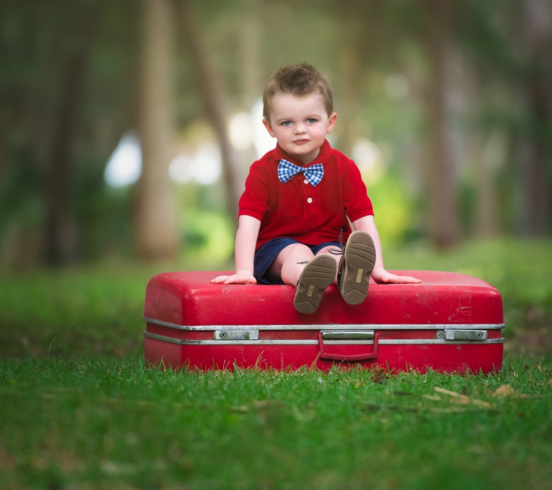 Das Cute Boy Sitting On Red Luggage Wallpaper 1080x960
